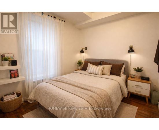 A bedroom with a large bed, a nightstand, and a window with sheer curtains.