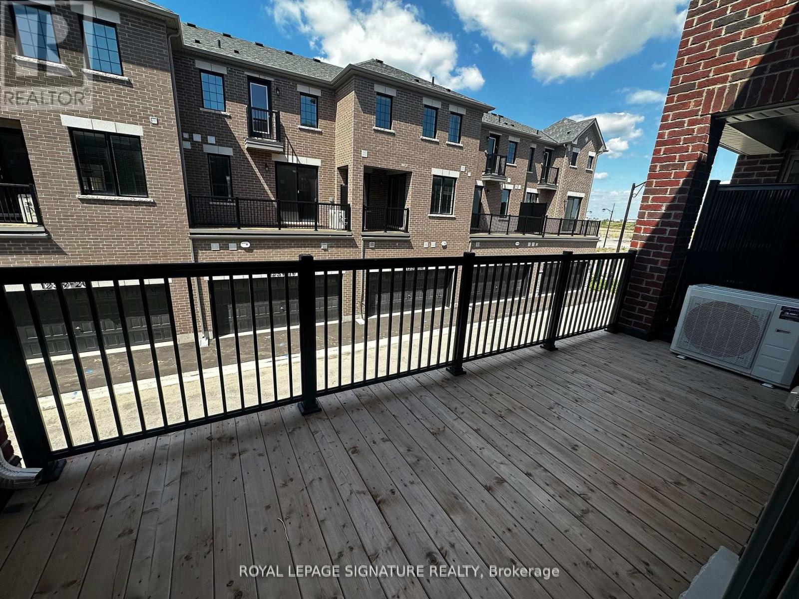 A wooden deck with a black railing in front of a brick building.
