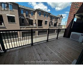 A wooden deck with a black railing in front of a brick building.
