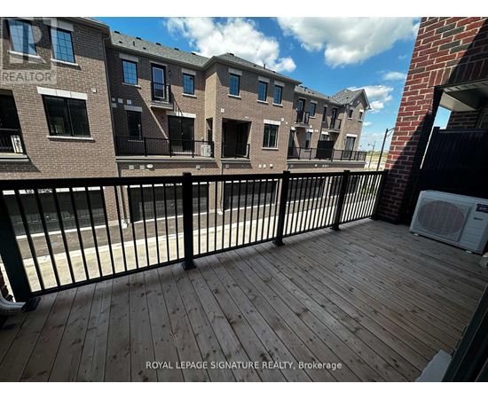 A wooden deck with a black railing in front of a brick building.