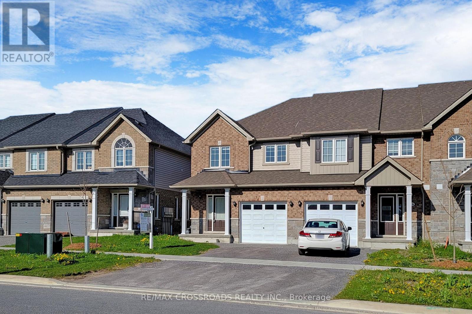 A white car is parked in front of a house with a RE/MAX sign.