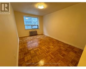 A room with wooden flooring and a window with a view of a building outside.