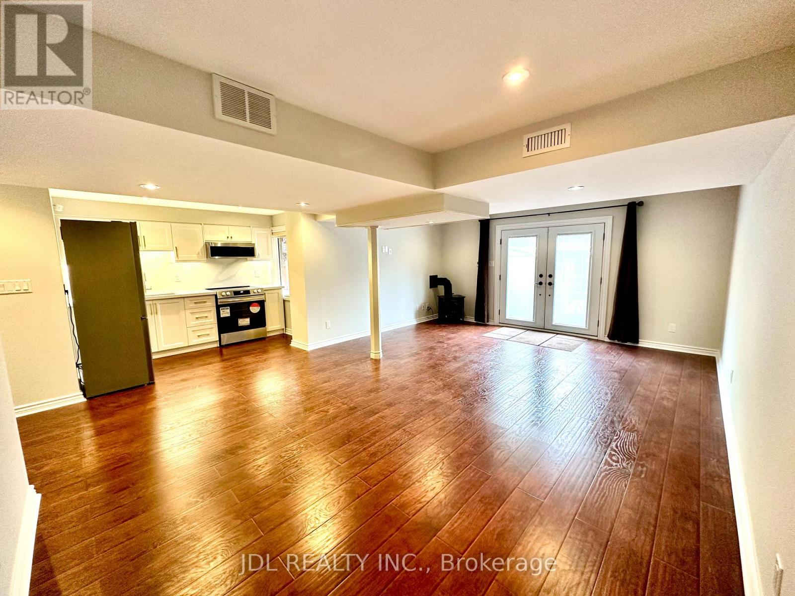 A spacious room with wooden flooring and a kitchen area in the background.