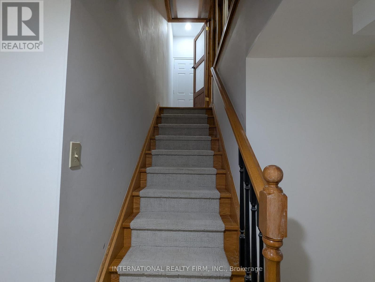 A staircase with a wooden handrail and grey carpeted steps.