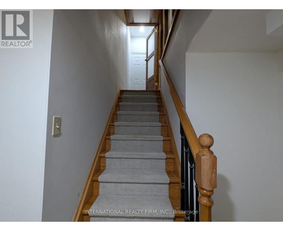 A staircase with a wooden handrail and grey carpeted steps.