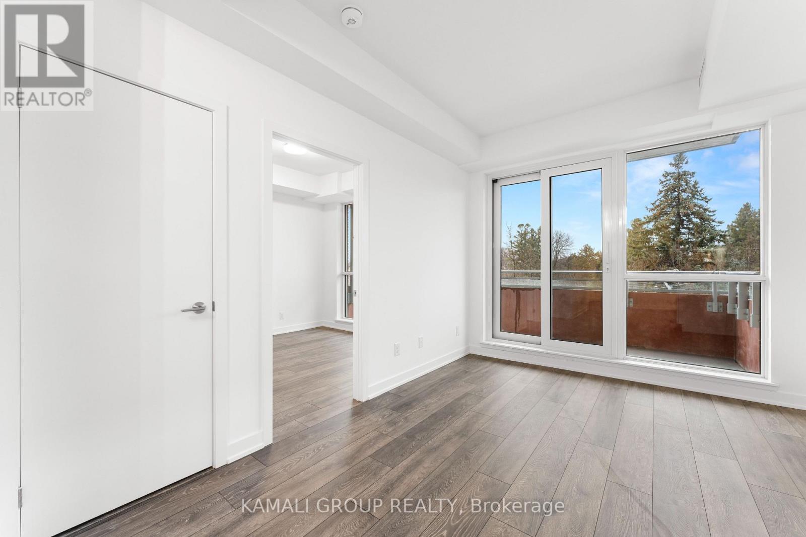 A room with a white door and a window with a view of trees outside.