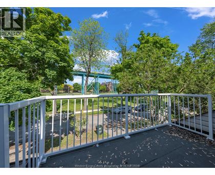 A balcony with a white railing and a view of a green bridge and trees.