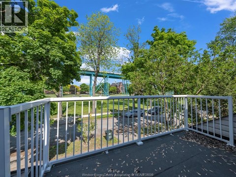 A balcony with a white railing and a view of a green bridge and trees.