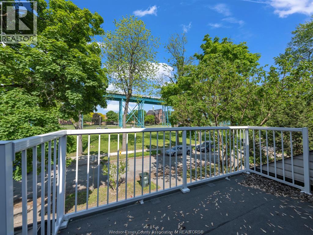 A balcony with a white railing and a view of a green bridge and trees.
