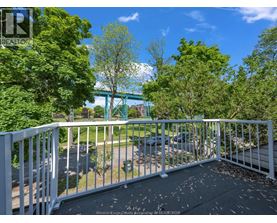 A balcony with a white railing and a view of a green bridge and trees.