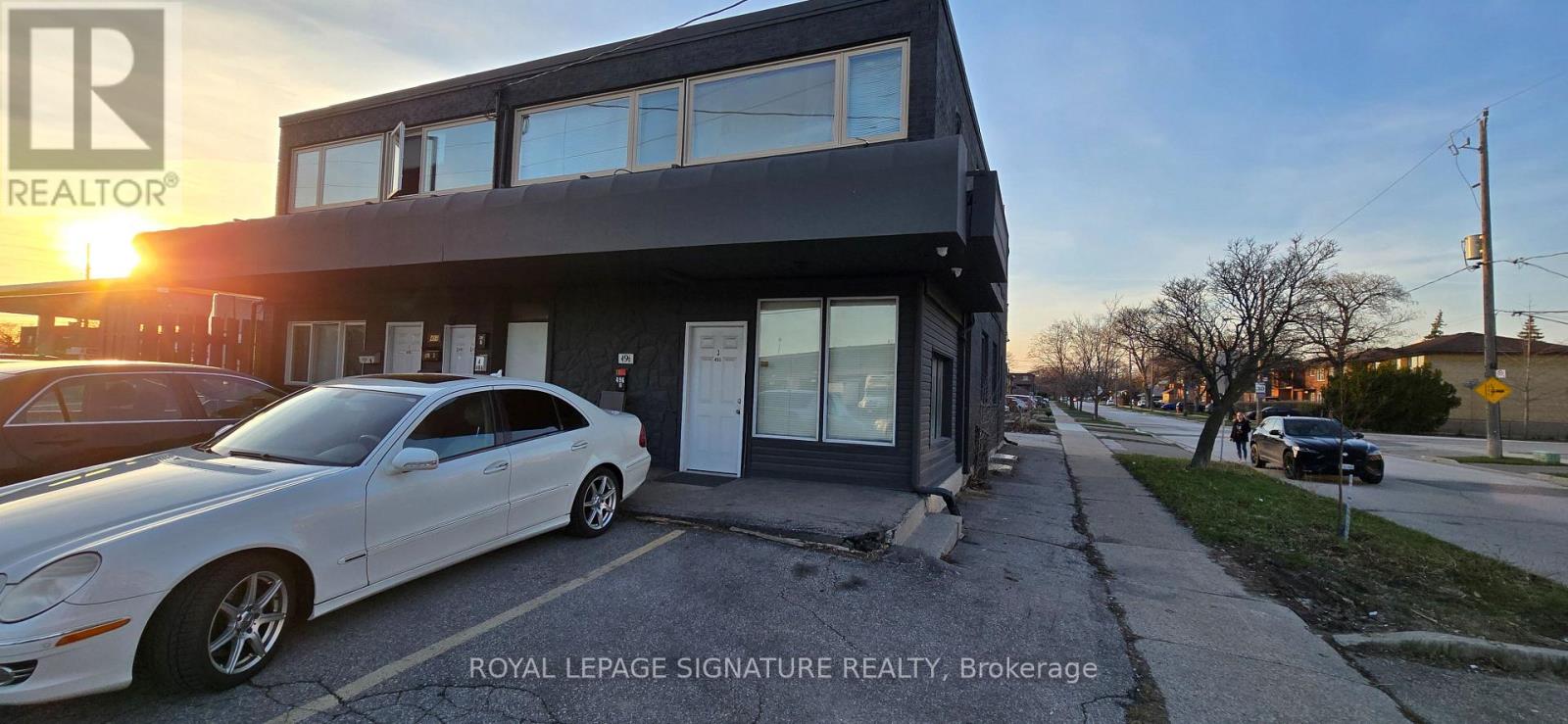 A white car is parked in front of a two-story building.