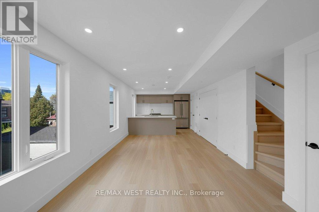 A spacious room with wooden flooring and white walls, with a staircase on the right side.