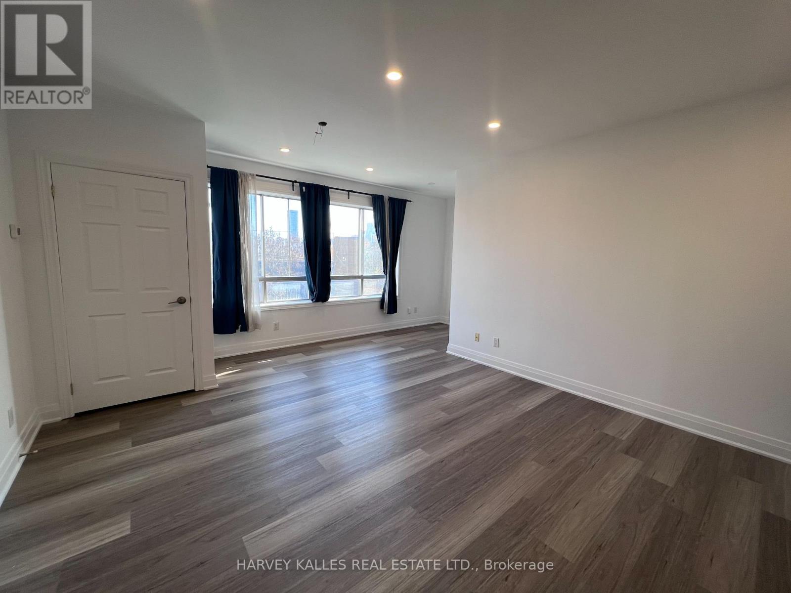 A spacious room with wooden flooring and a large window with curtains.