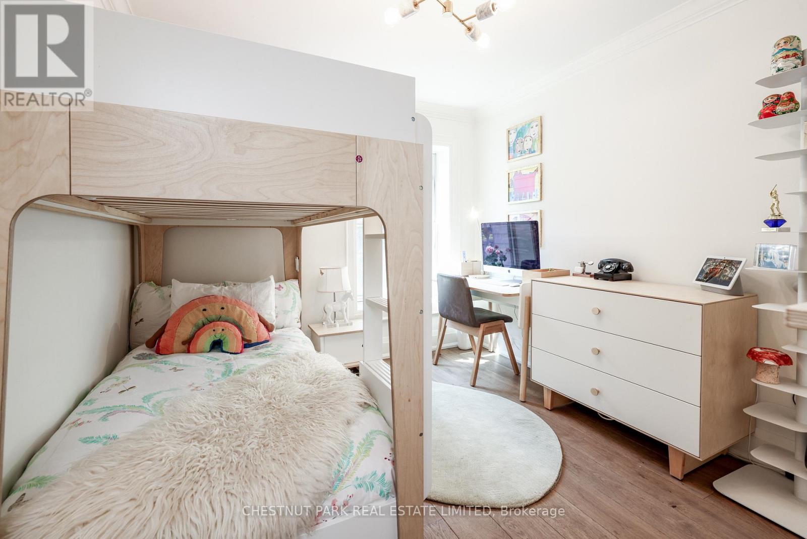 A bedroom with a white bed, a desk with a chair, and a white dresser with shelves.