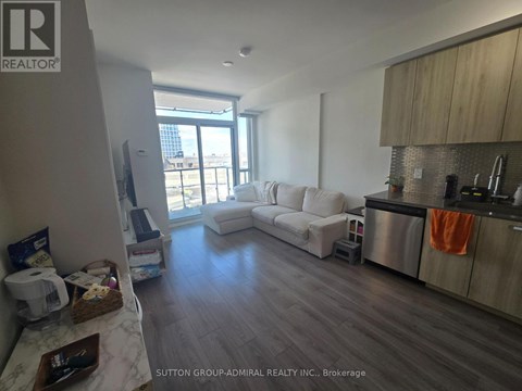 A living room with a white couch and a kitchen area with a stainless steel refrigerator.