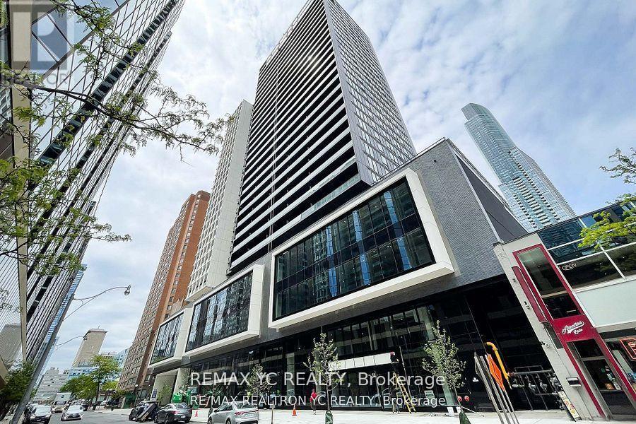 A tall building with a glass facade stands in front of a tree.