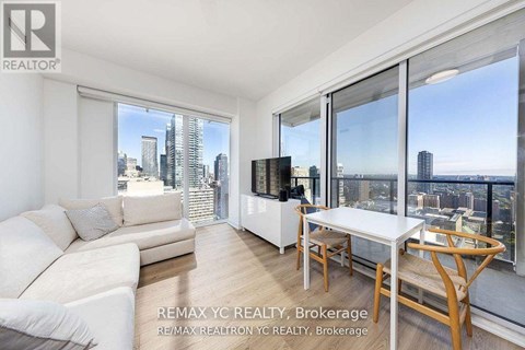 A living room with a couch, chair, and table with a city view through the windows.