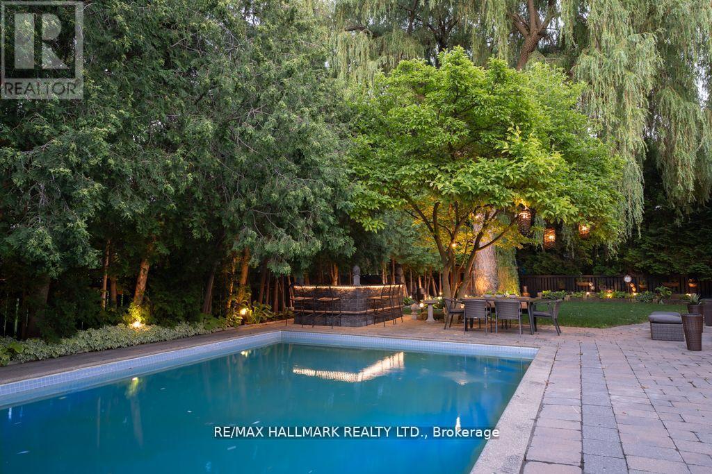 A pool surrounded by trees and a patio area with chairs and a table.