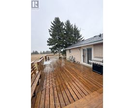 A wooden deck with a bench and a grill on a cloudy day.