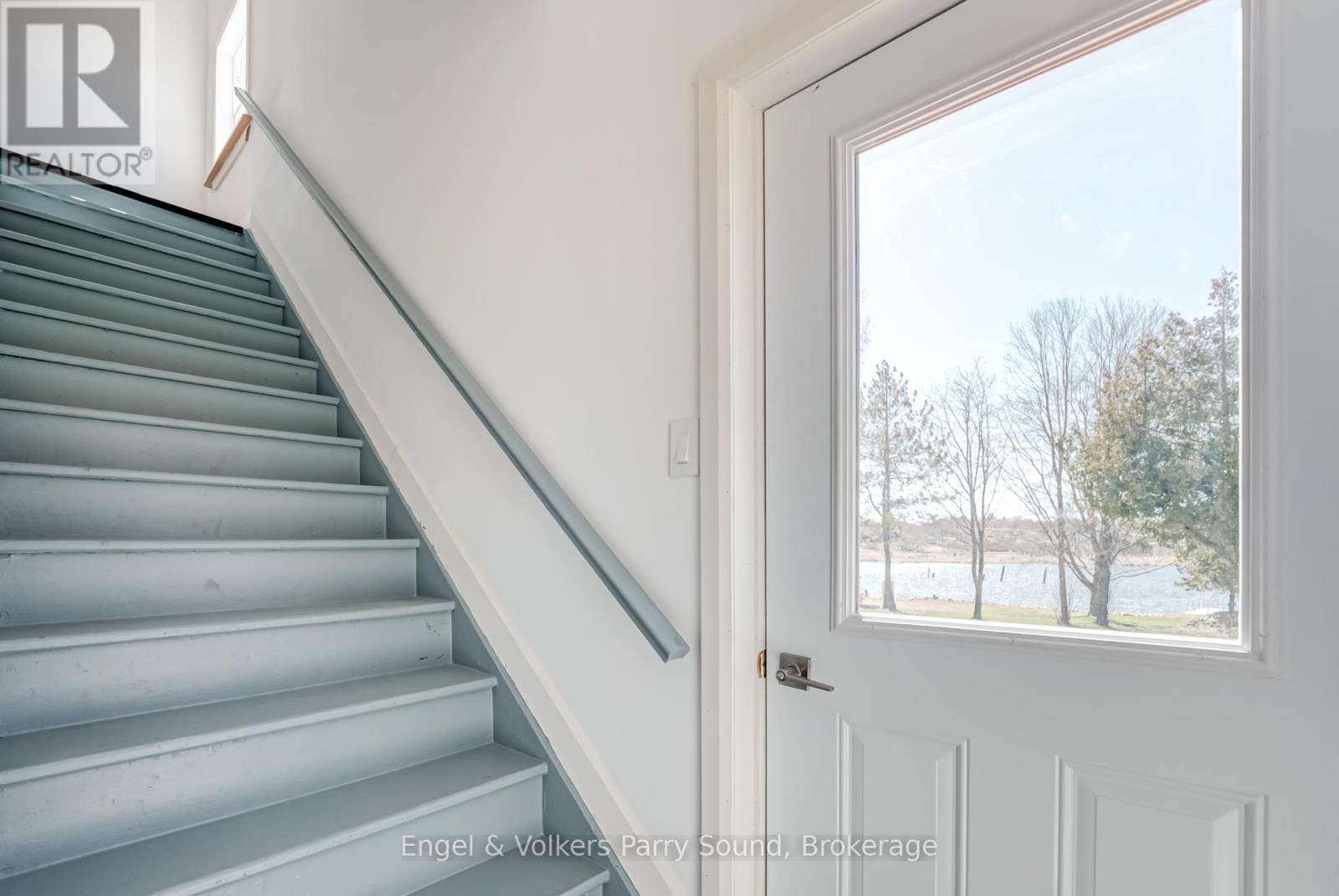 A staircase with a white door and a window showing a view of trees and a body of water.