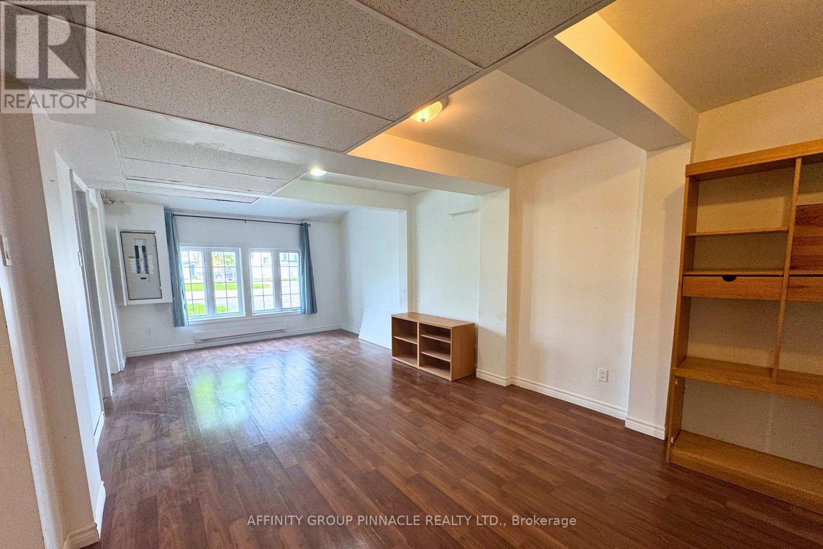 A spacious room with wood flooring and a large window.