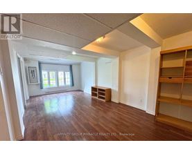 A spacious room with wood flooring and a large window.