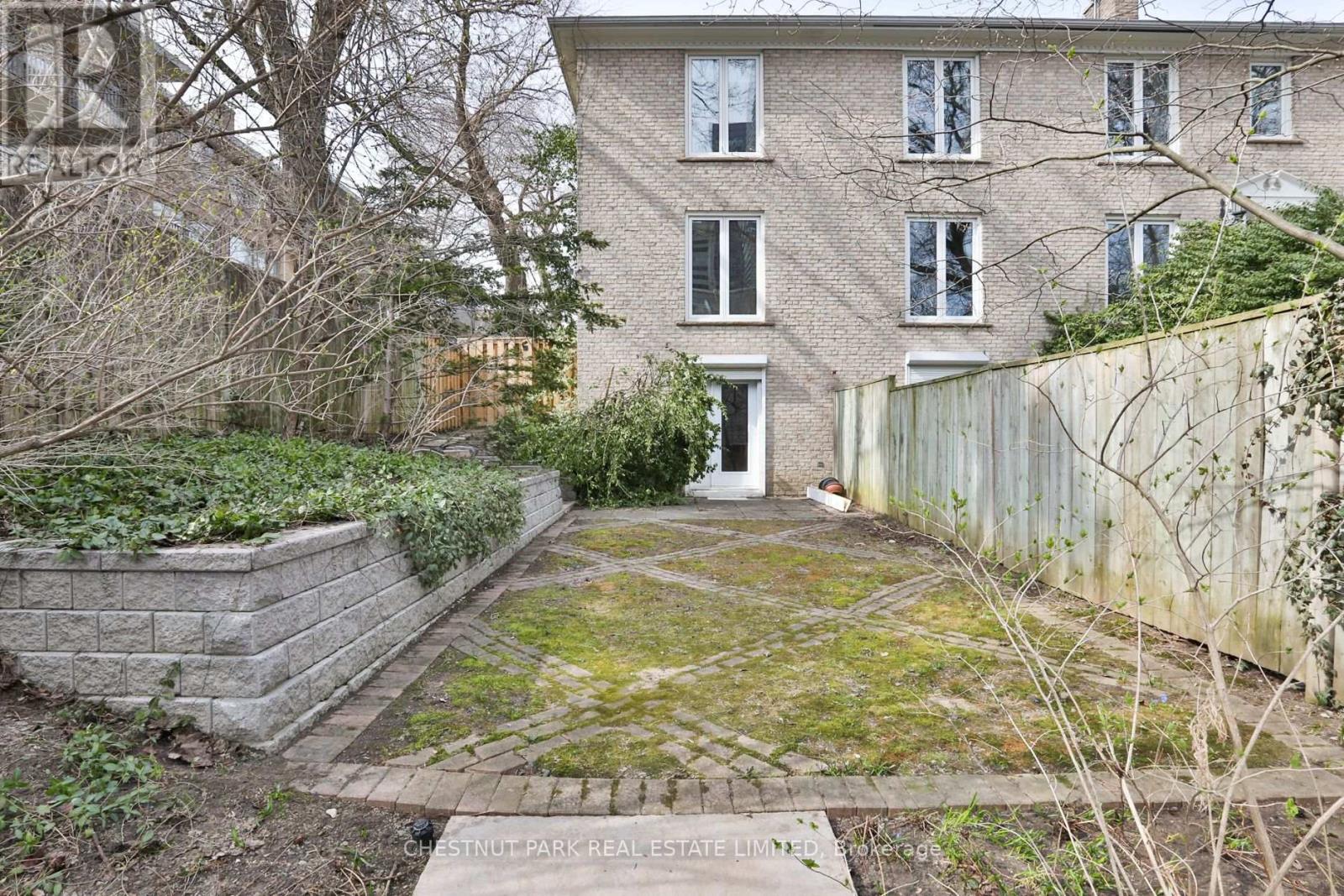 A brick building with a white door and windows is surrounded by a fence and a small garden.