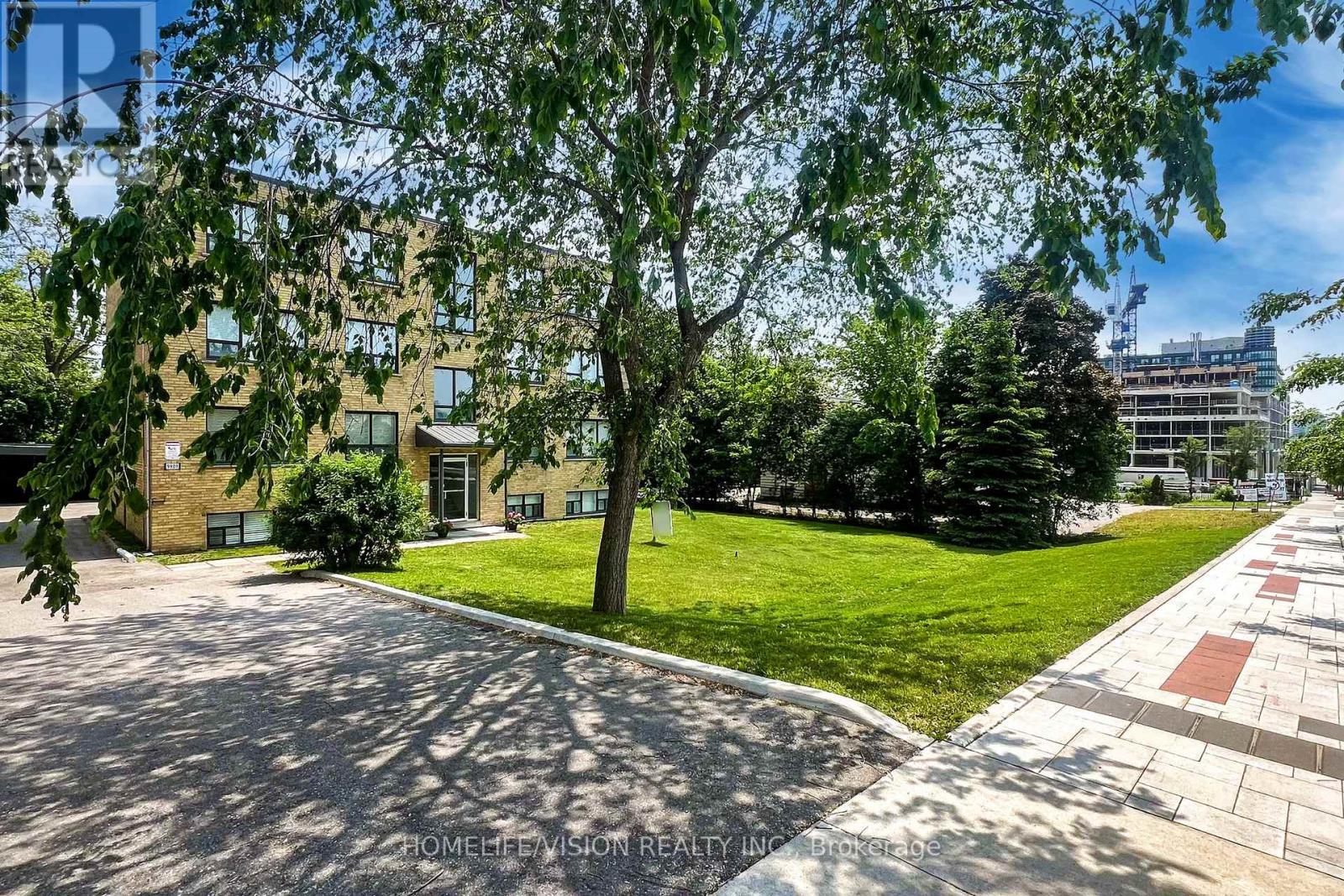 A sunny day at a residential area with a building, trees, and a paved walkway.