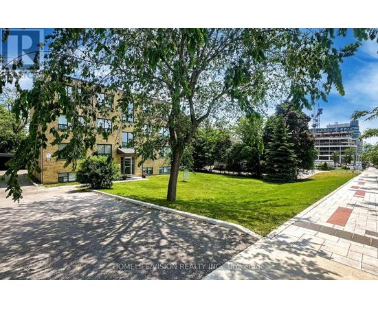 A sunny day at a residential area with a building, trees, and a paved walkway.