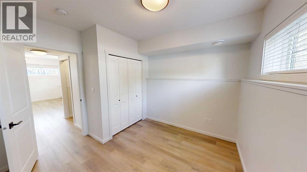 A white bedroom with a wooden floor and a window with blinds.