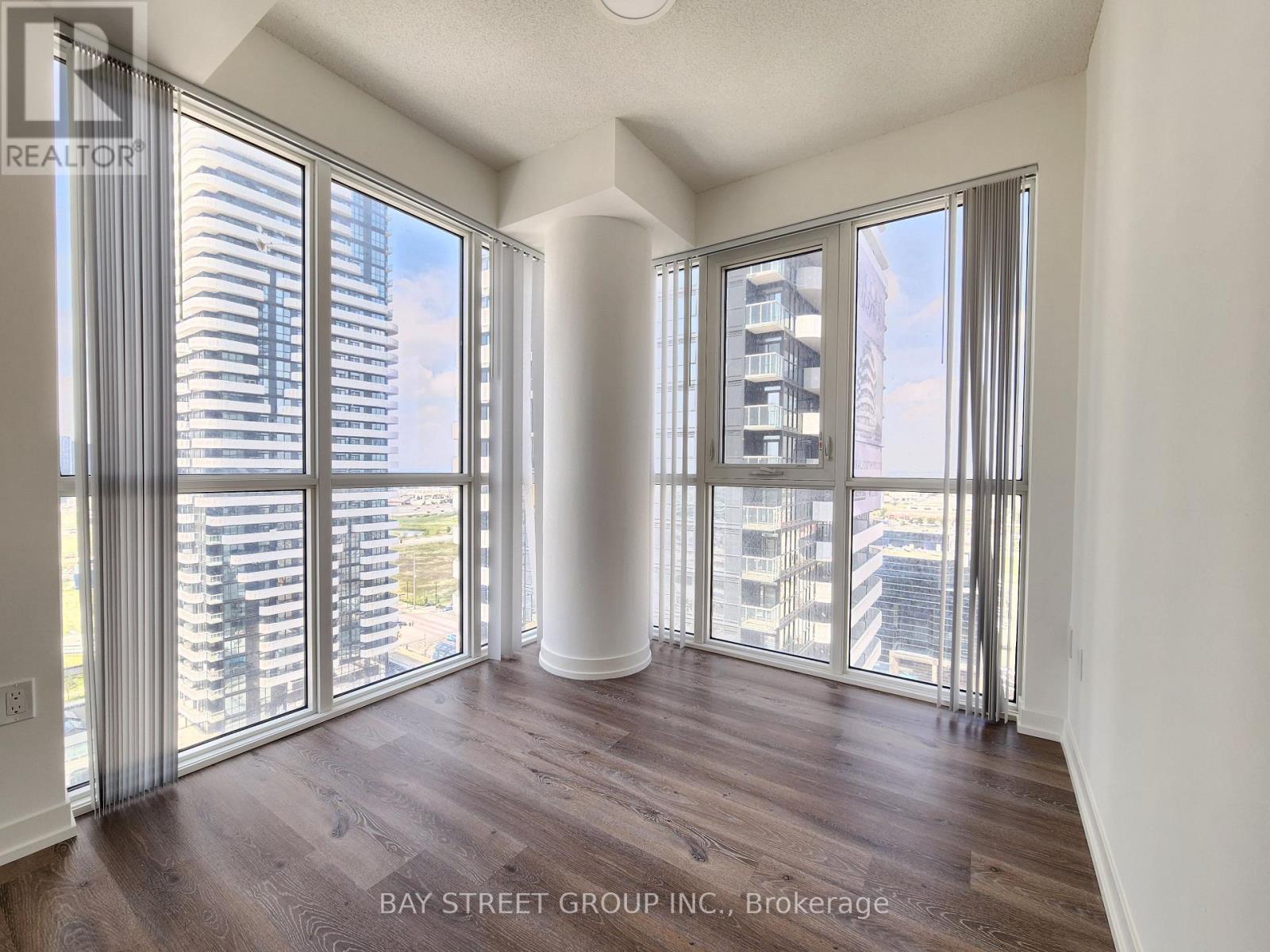 A spacious room with wooden floors and large windows overlooking a cityscape.