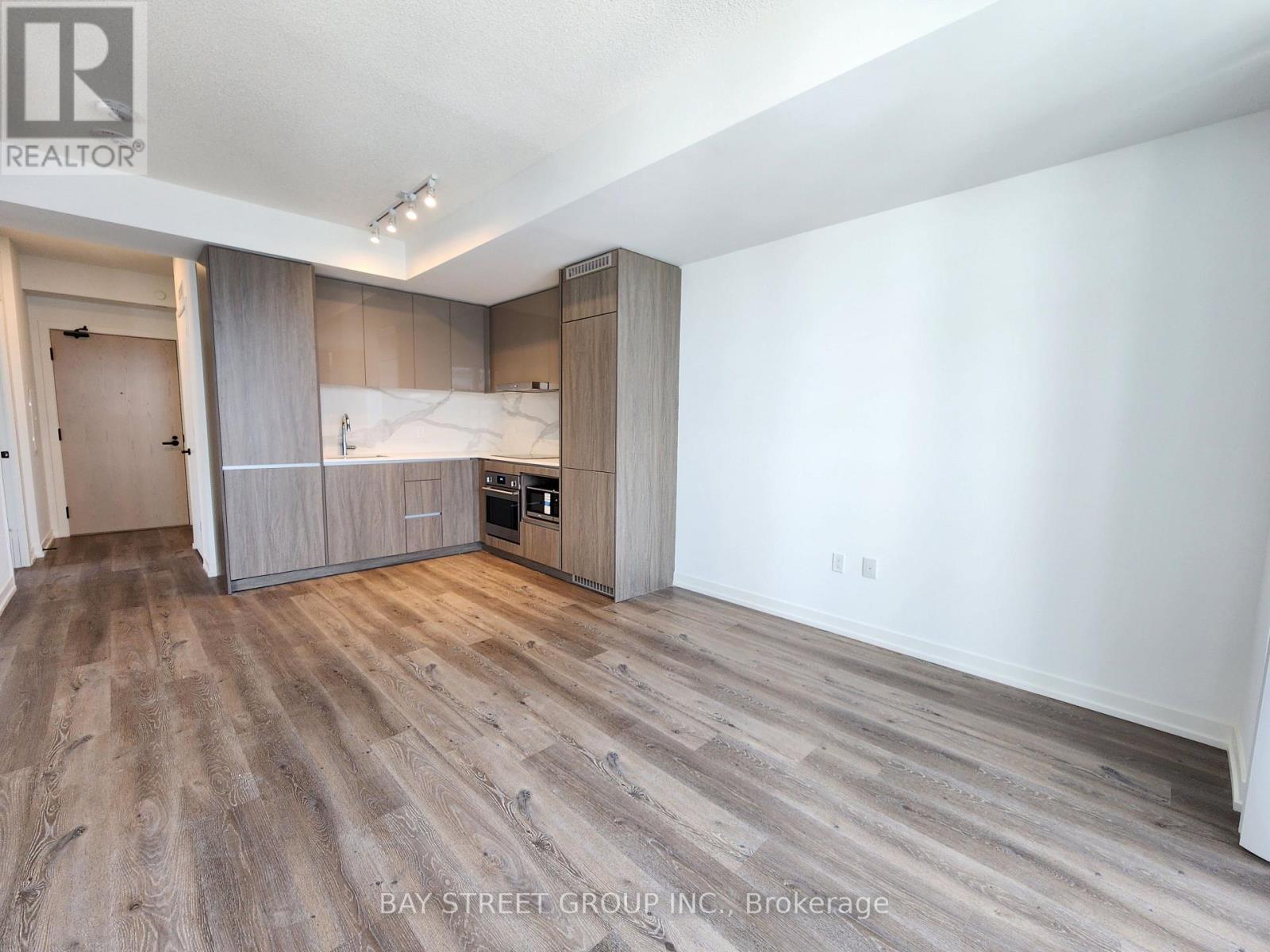 A spacious kitchen with wooden flooring and a white wall.