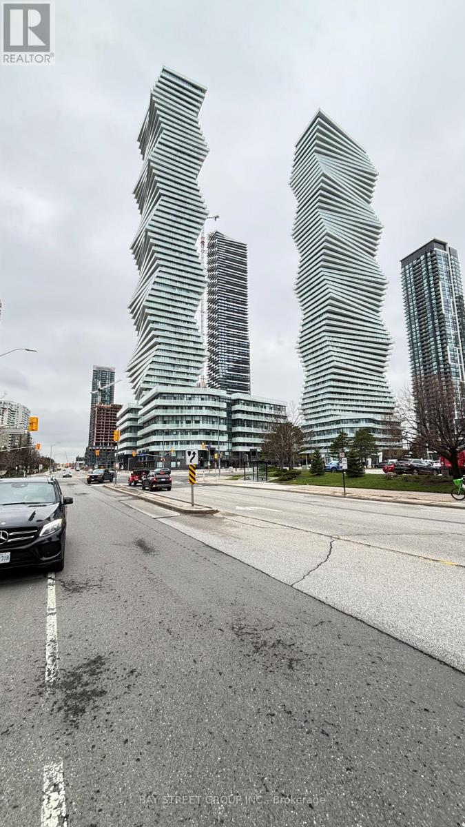 A tall, slender building with a curved design stands in front of a building with a flat roof.