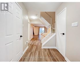 A hallway with a wooden floor and white walls leading to a staircase.