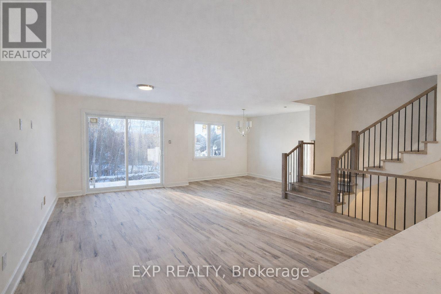 A spacious room with a staircase and a view of the outdoors through the windows.