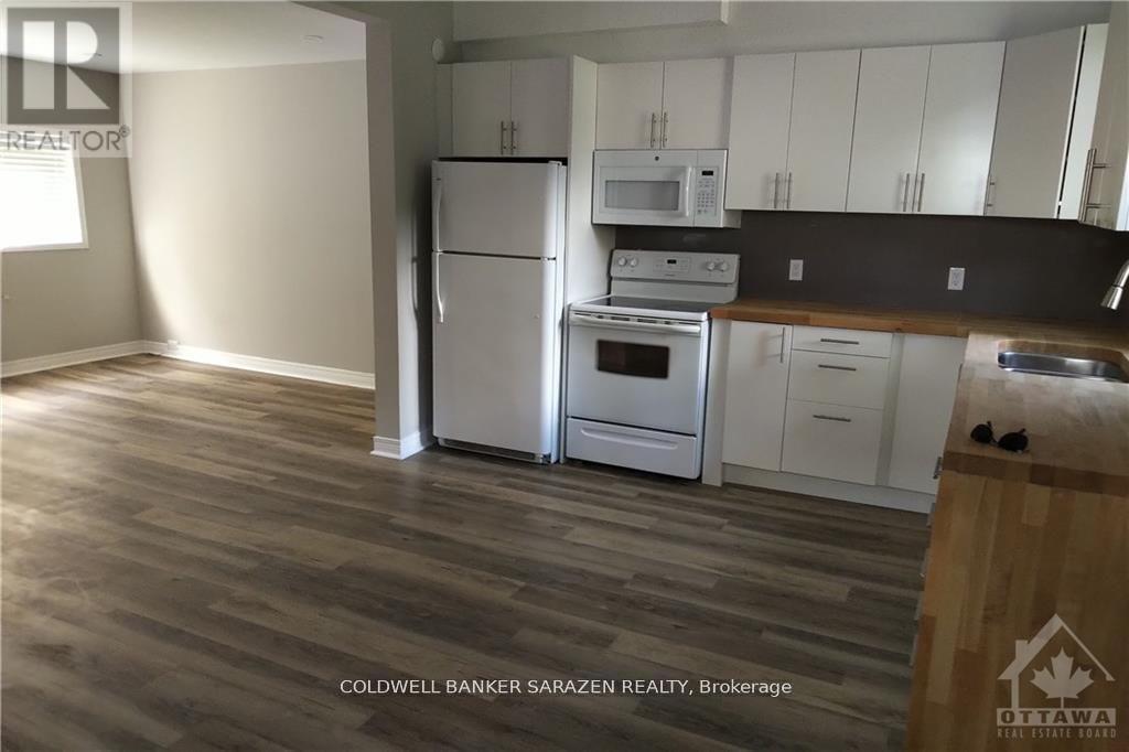A kitchen with white appliances and cabinets, and a wooden floor.