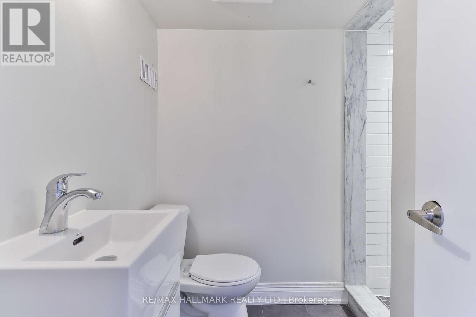 A white bathroom with a toilet, sink, and marble tiles.