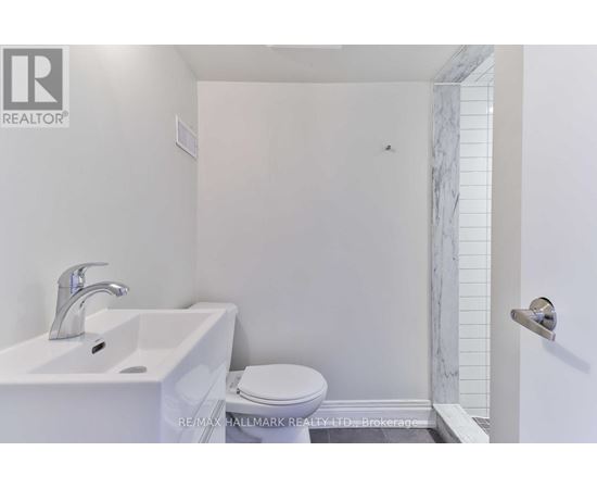 A white bathroom with a toilet, sink, and marble tiles.