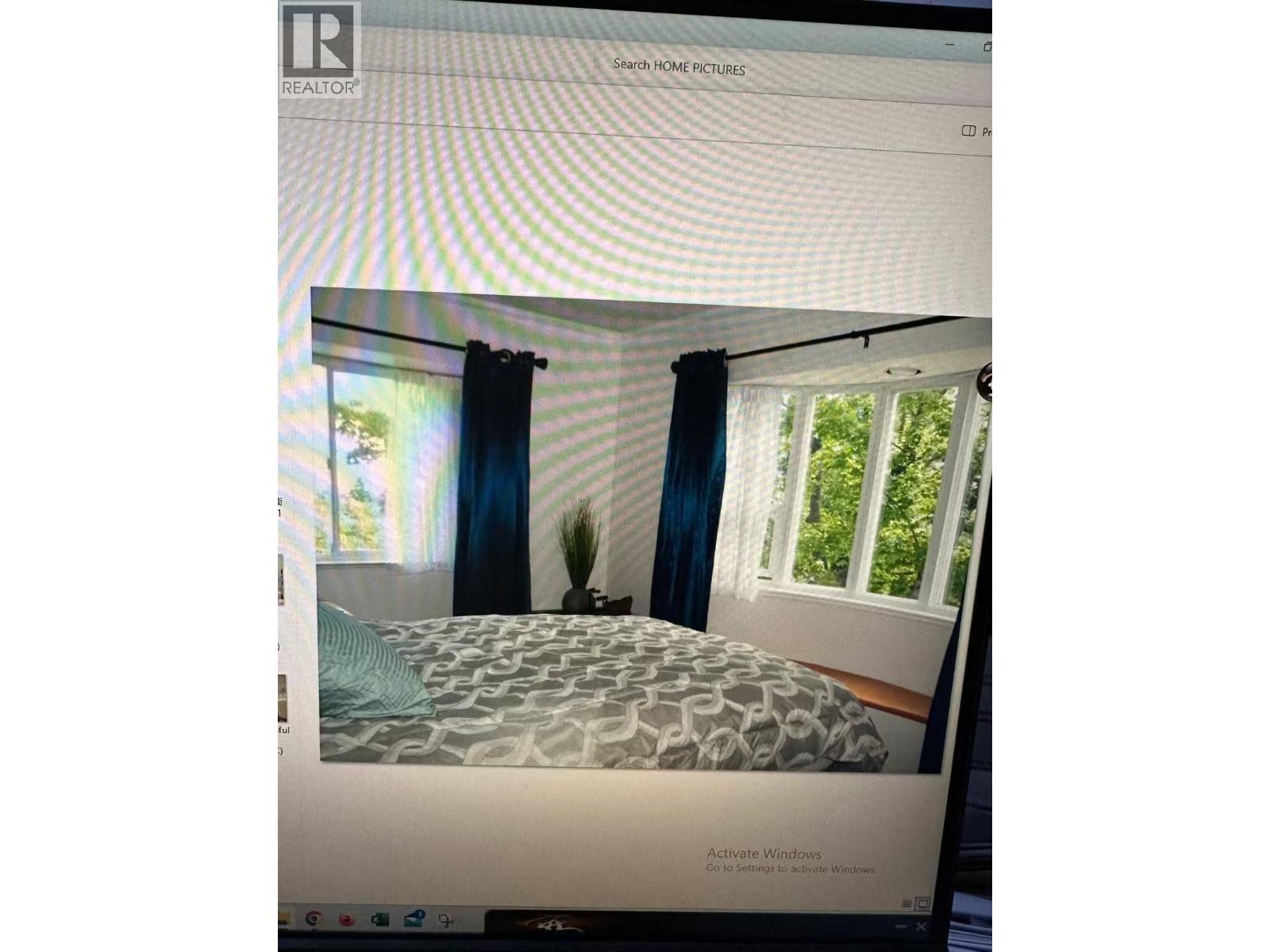 A bedroom with a bed, a window with blue curtains, and a plant on the windowsill.