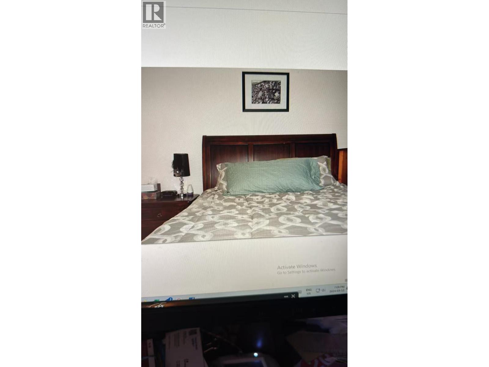 A bed with a green pillow and a picture frame on the wall.