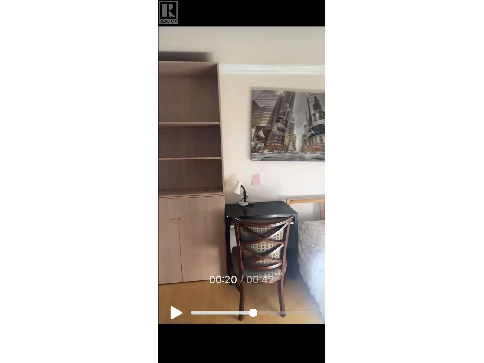 A black chair with a woven seat and back is in the foreground of a video.