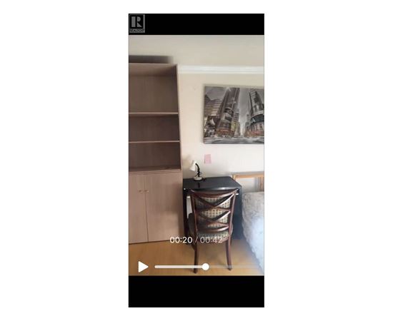 A black chair with a woven seat and back is in the foreground of a video.