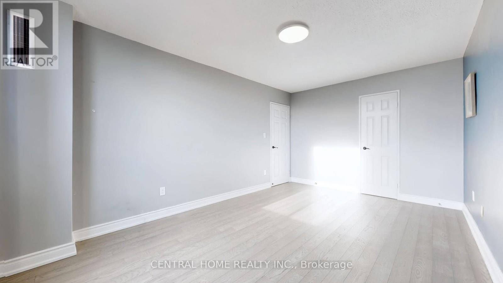 A spacious room with light wood flooring and white walls.