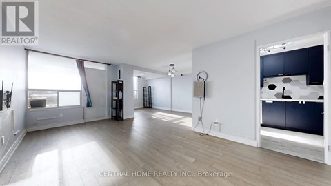 A spacious room with a large window and a kitchen area with a sink and stove.