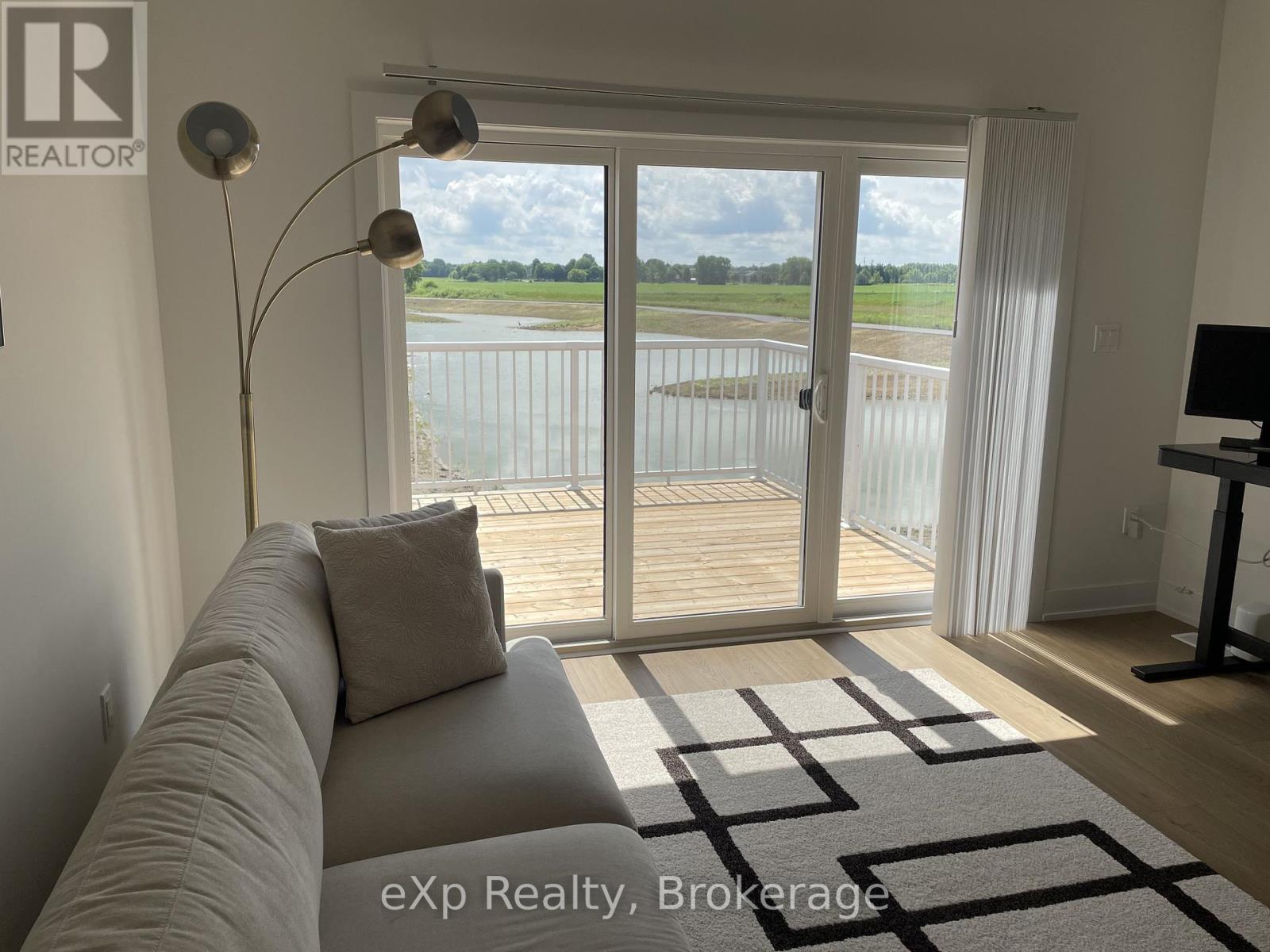 A living room with a grey couch and a large window with a view of a lake.