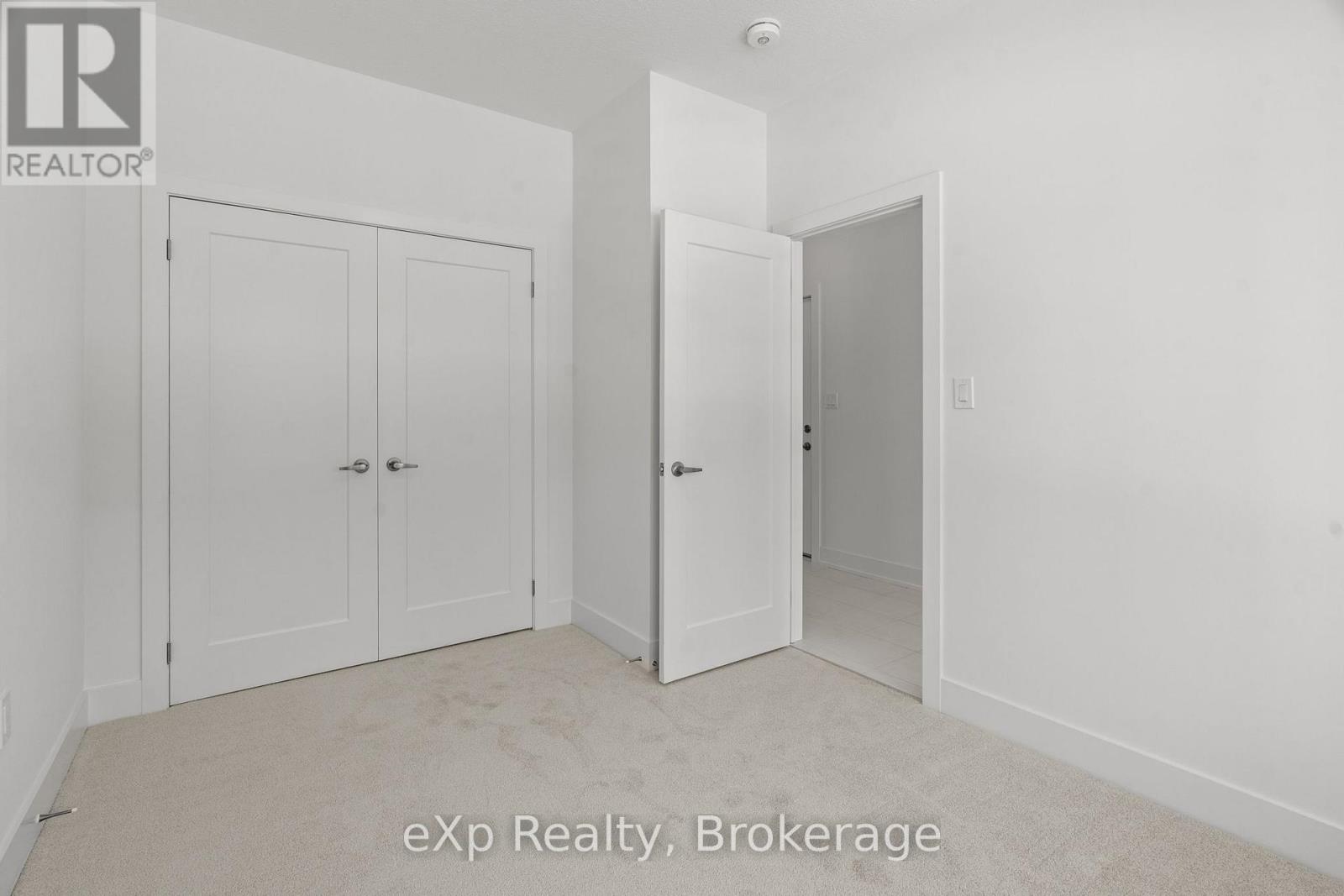 A white bedroom with a carpet floor and two doors.