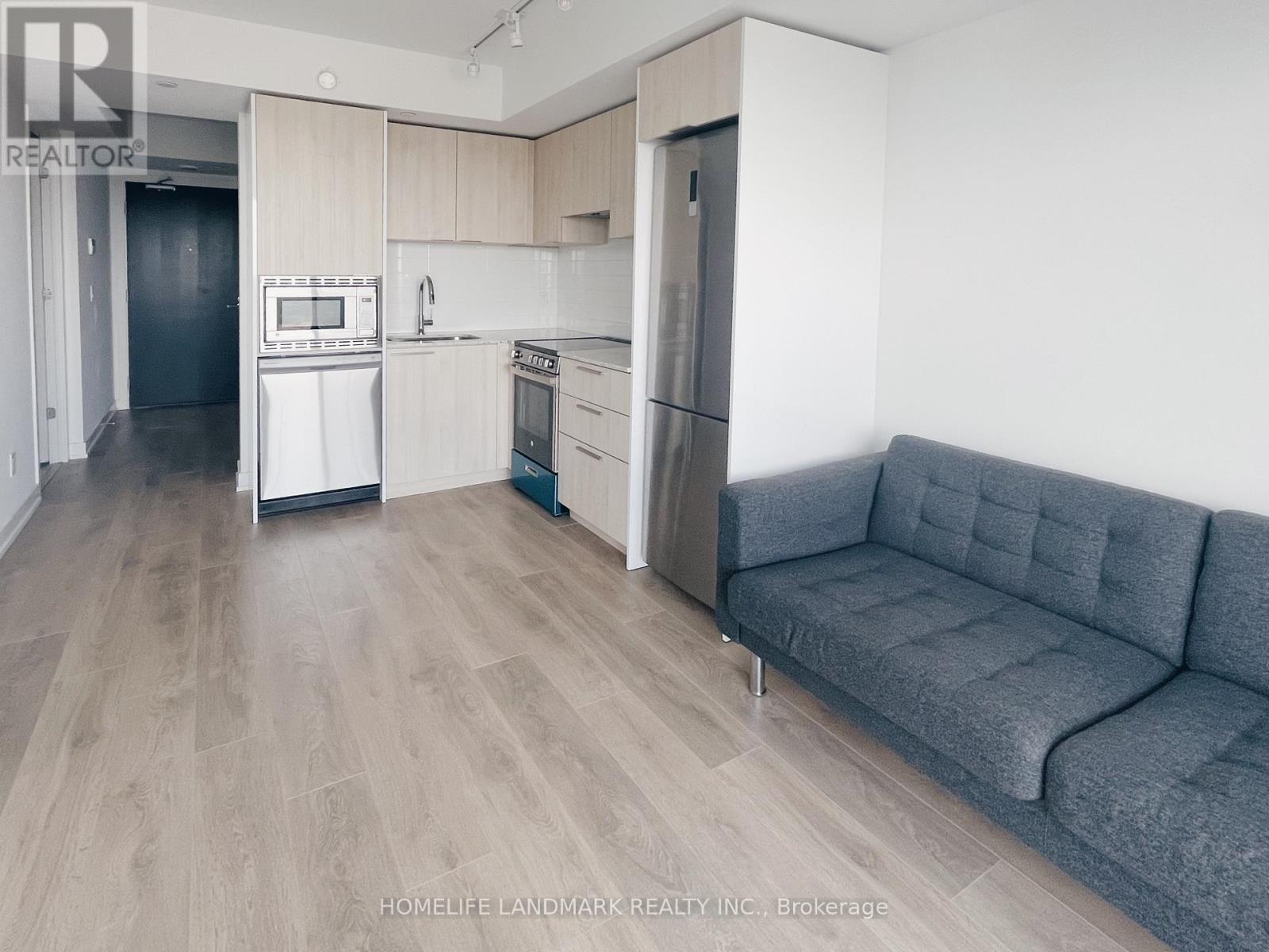 A living room with a grey couch and a kitchen area in the background.