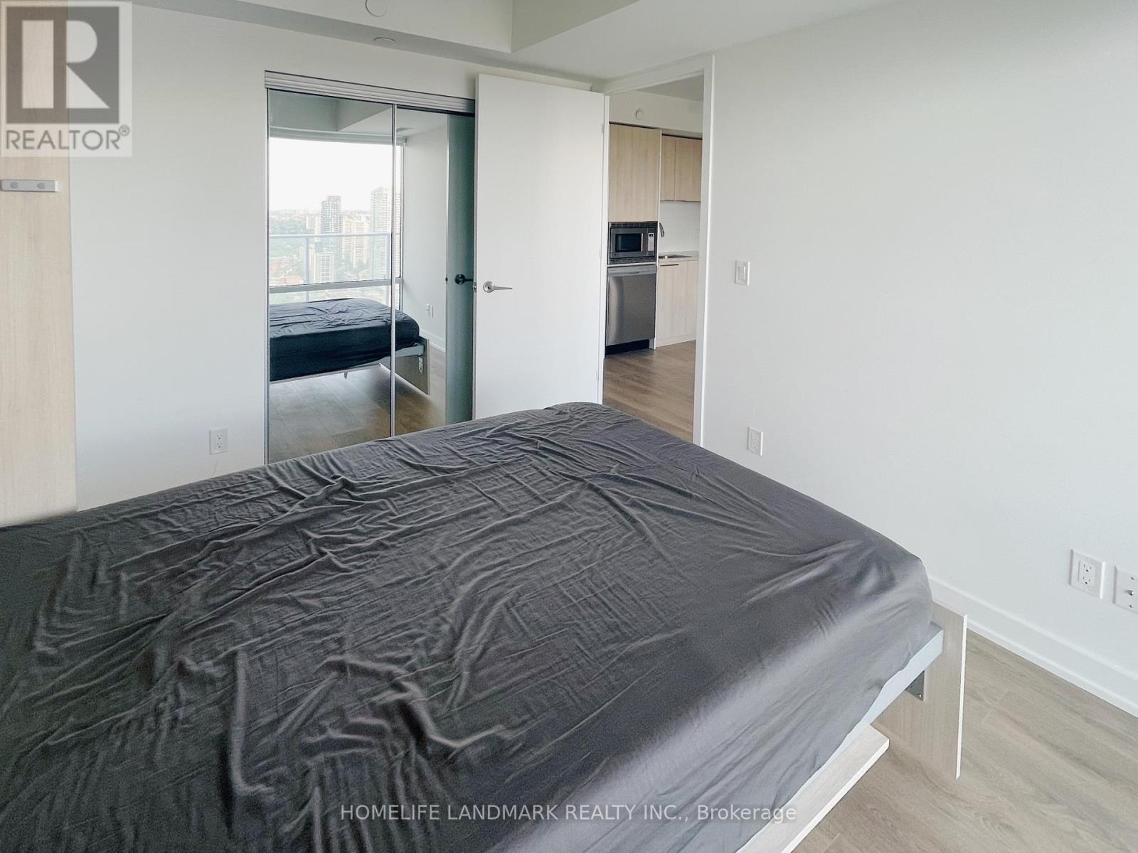A bedroom with a bed, a small kitchen, and a door leading to a balcony.