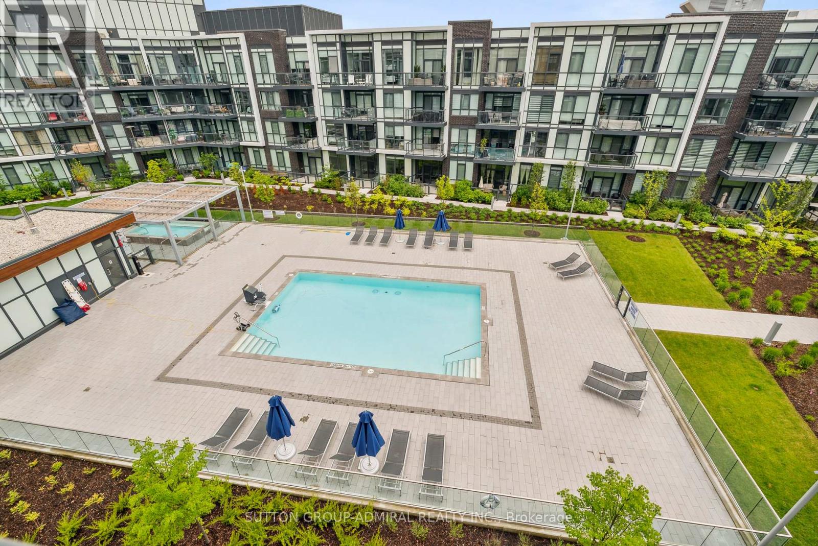 A swimming pool surrounded by a glass fence and lounge chairs.