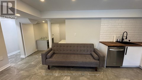 A grey couch sits in a spacious living room with a kitchen area in the background.